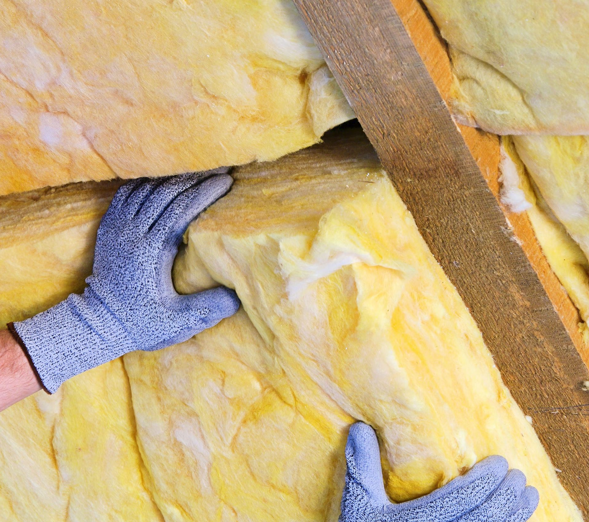 Mains gantées, installant de l'isolant entre des poutres en bois.