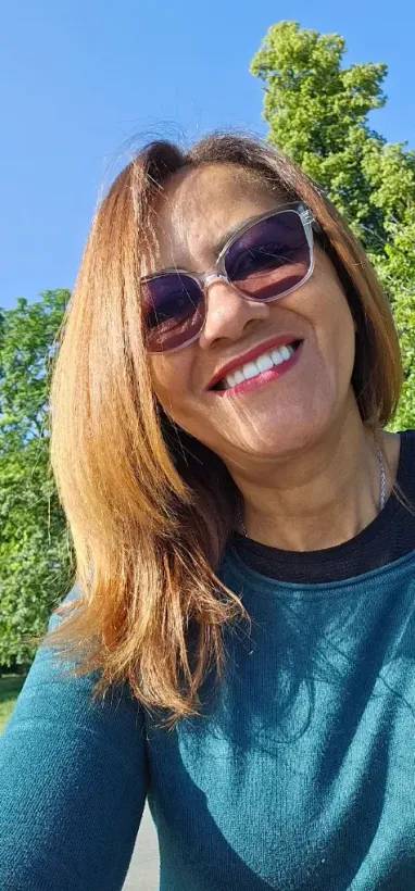 Une personne souriante, portant des lunettes de soleil et une chemise turquoise, 