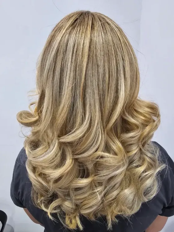 Vue de dos de cheveux blonds mi-longs avec des boucles souples et des racines foncées