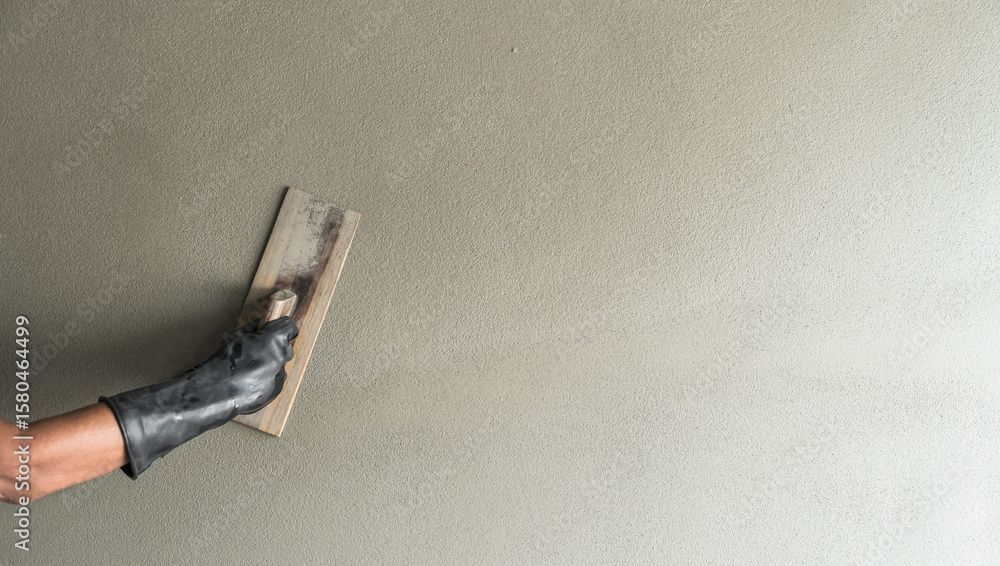Eine Hand in einem schwarzen Handschuh glättet mit einer Kelle den nassen Putz an der Wand.