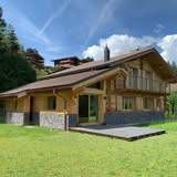 Chalet en bois avec pelouse verte, se détachant sur un ciel ensoleillé.