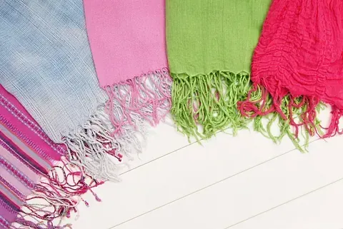 Un grupo de bufandas de colores están colocadas una encima de otra sobre una superficie blanca.