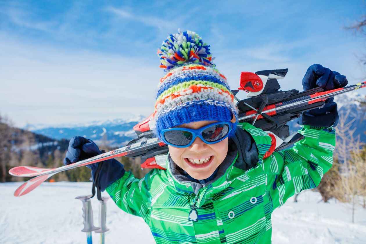 Enfant souriant portant des skis sur ses épaules