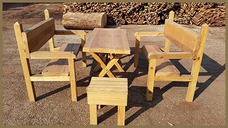 Un conjunto de sillas de madera y una mesa frente a una pila de troncos.