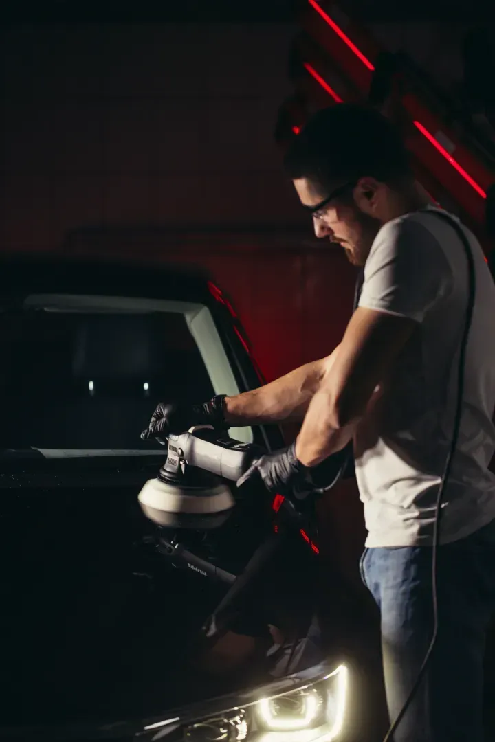 Un hombre está puliendo un coche con una máquina en una habitación oscura.