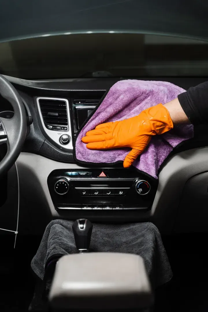 Una persona está limpiando el interior de un coche con una toalla y guantes.