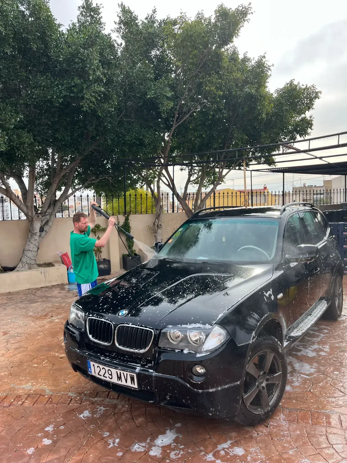 Un hombre está lavando un BMW negro con una manguera.