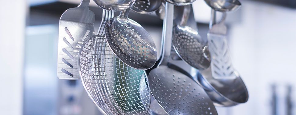 Ein Bündel Küchenutensilien aus Edelstahl hängt an einem Gestell.