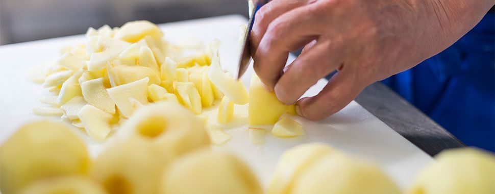 Eine Person schneidet Kartoffeln auf einem Schneidebrett.