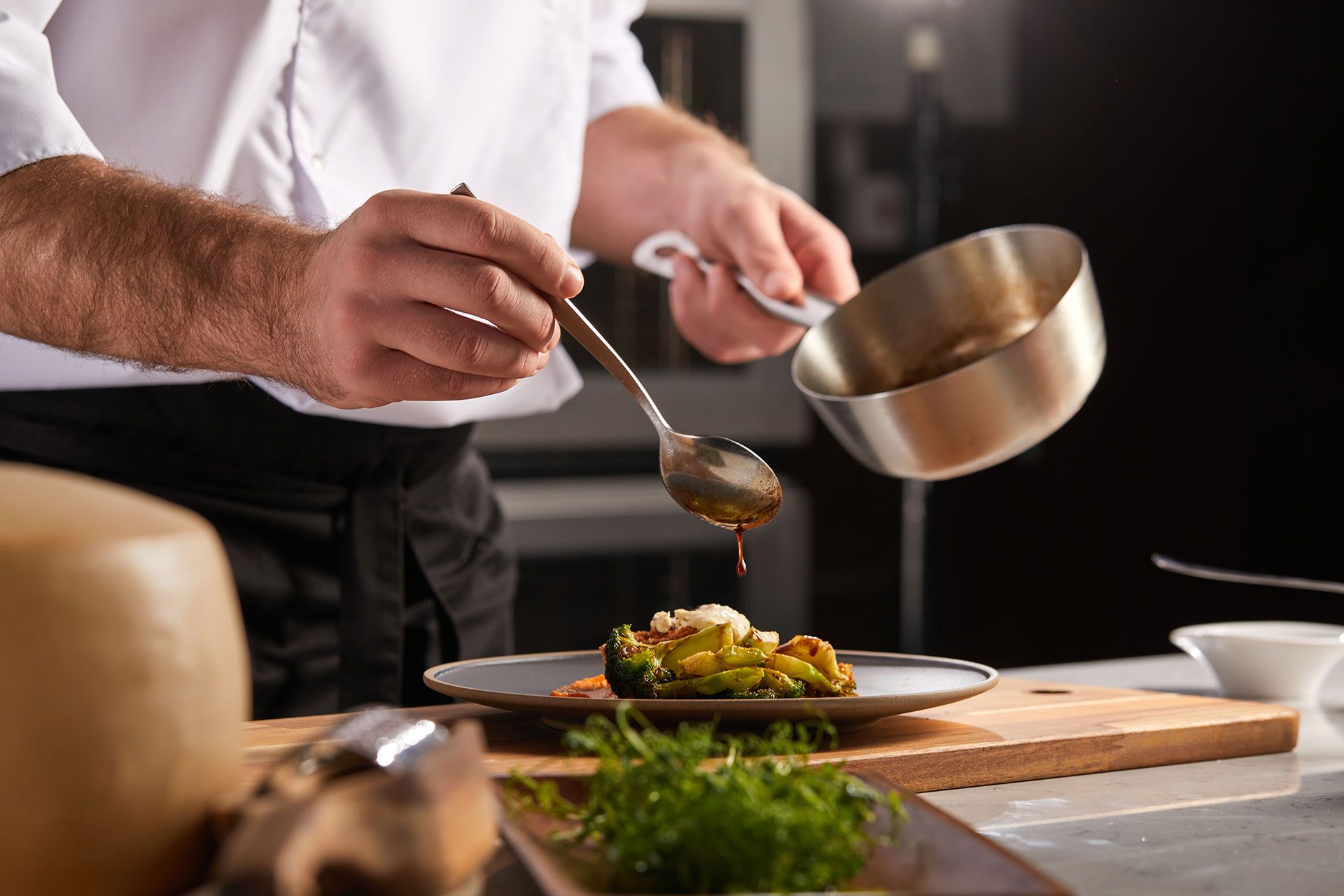 Ein Koch gießt mit einem Löffel Soße auf einen Teller mit Essen.