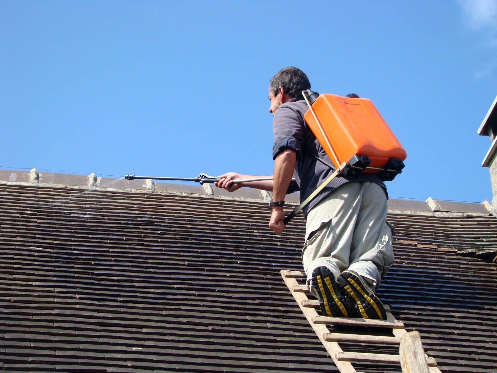 Couvreur nettoyant une toiture avec un pulvérisateur