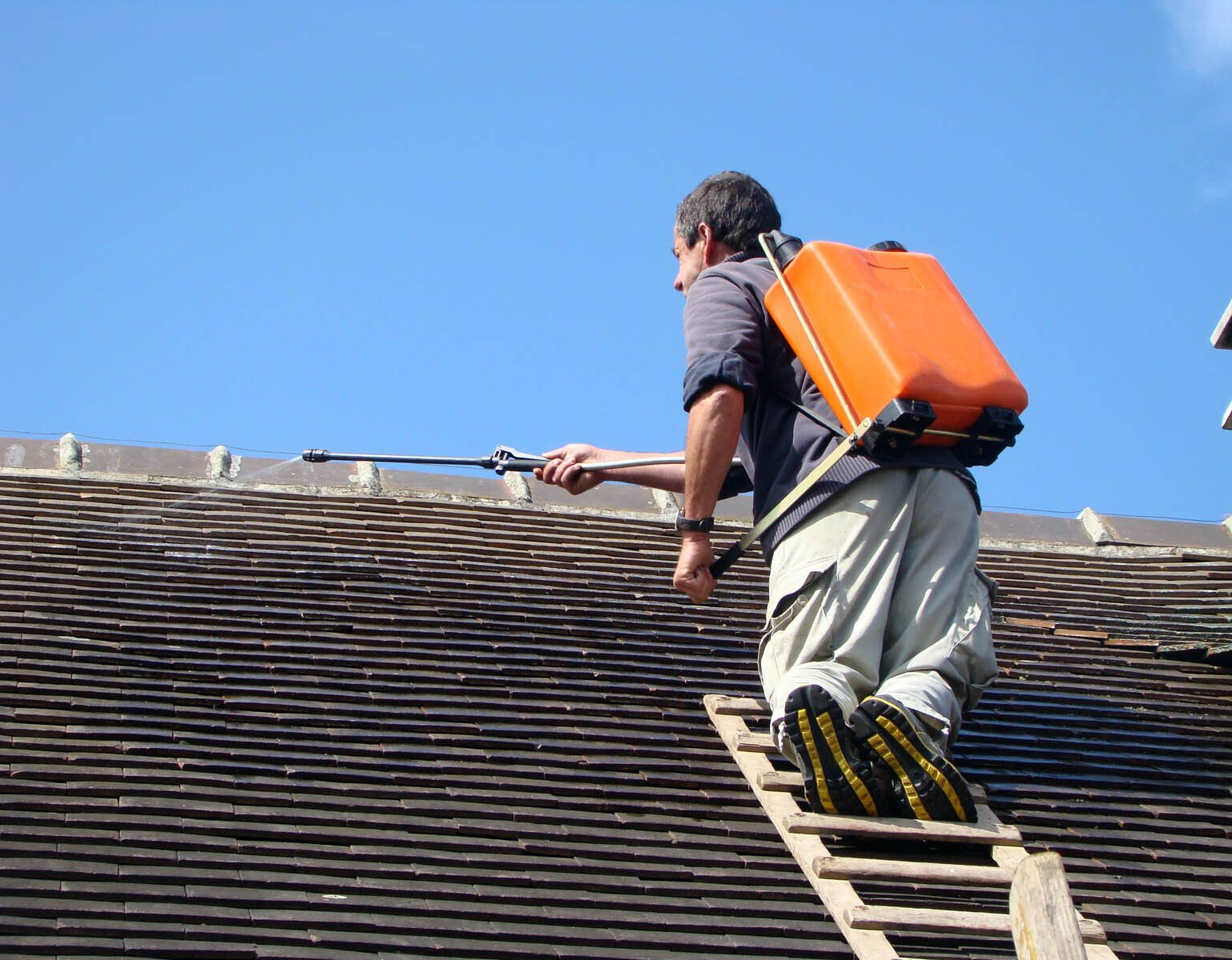 Couvreur nettoyant une toiture avec un pulvérisateur