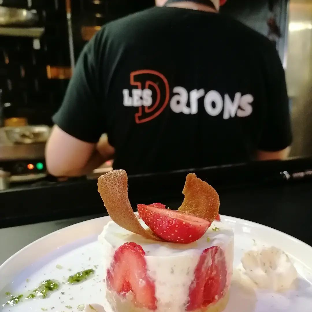 Dessert aux fraises dans une assiette, chef en chemise noire en arrière-plan.