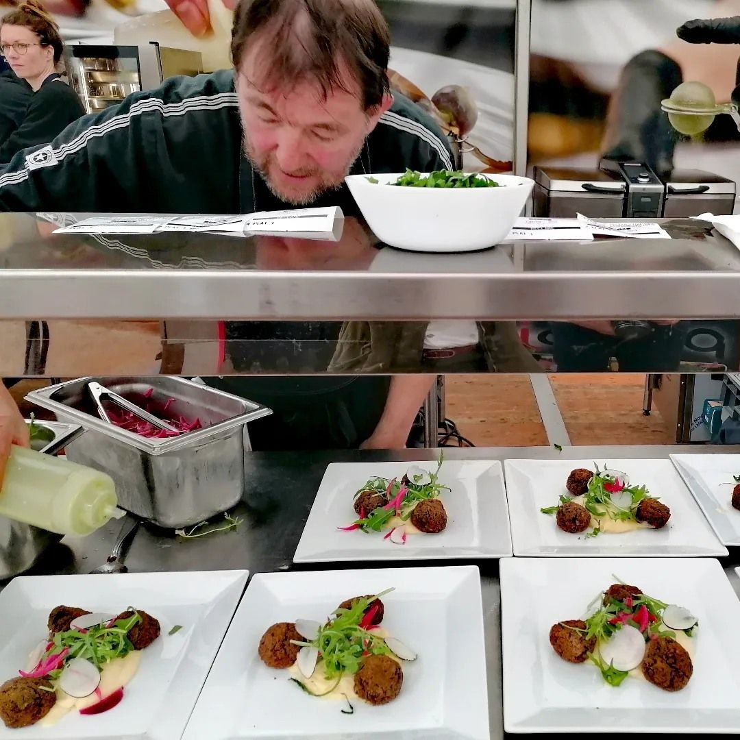 Le chef dresse les assiettes avec une expression concentrée, plusieurs assiettes d'amuse-gueules.