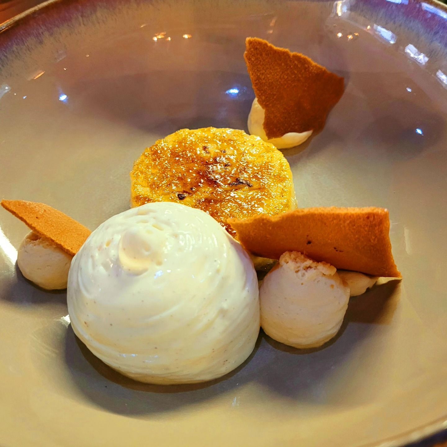Dessert : Crème brûlée, crème fouettée et biscuits croustillants dans un bol beige.