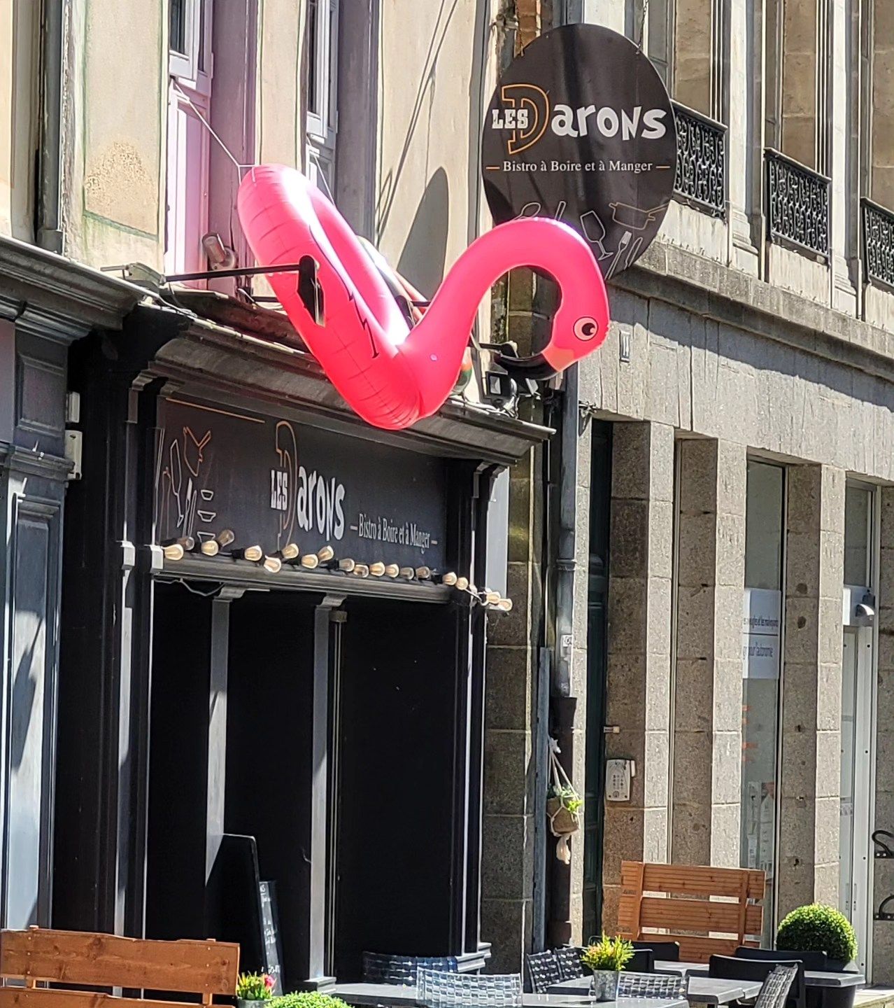 Un flamant rose gonflable est suspendu au-dessus de l'entrée d'un restaurant, au-dessus de l'enseigne. Vue extérieure.