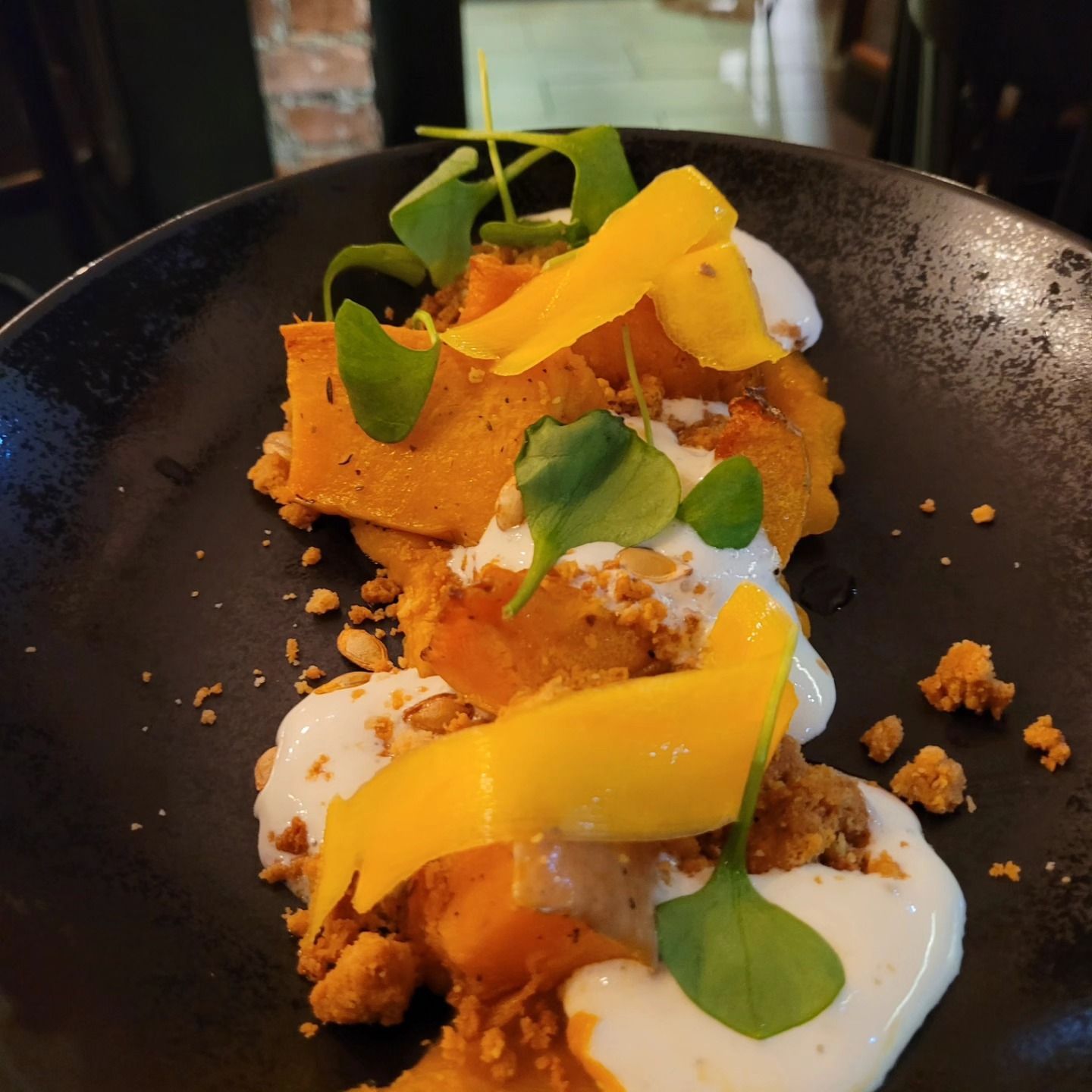 Assiette de courge rôtie avec mangue, crème et légumes verts.