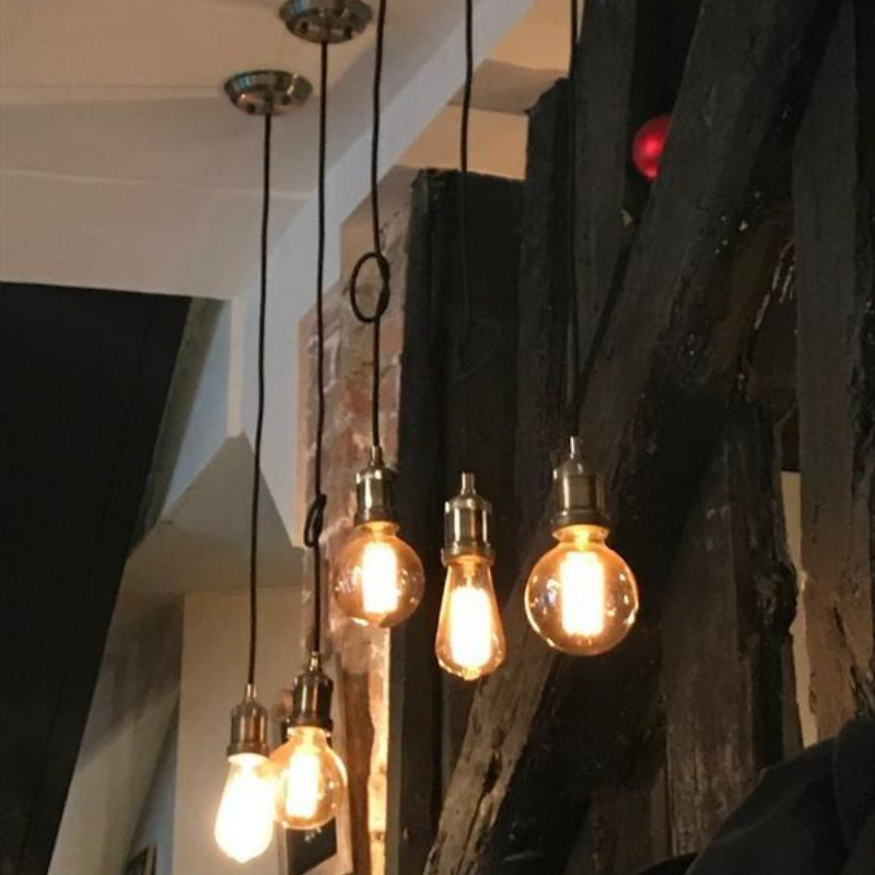 Cinq ampoules suspendues de style Edison, fixées à un plafonnier, dans un intérieur rustique aux poutres en bois.