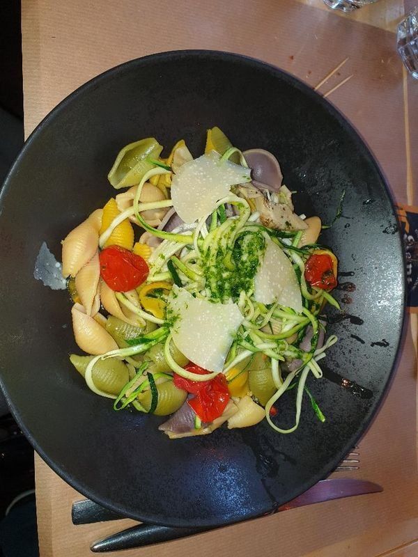 Plat de pâtes aux courgettes, tomates et parmesan, servi sur une assiette noire.