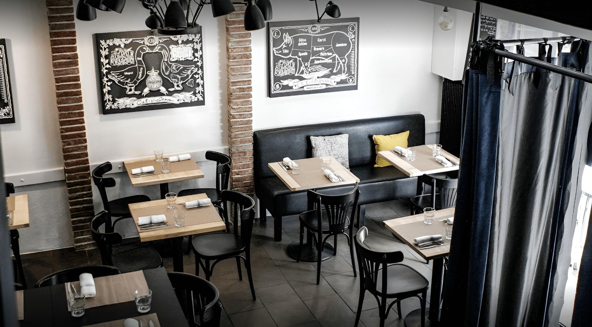 Intérieur d'un restaurant avec tables, chaises, banquette noire, œuvres d'art et rideaux.