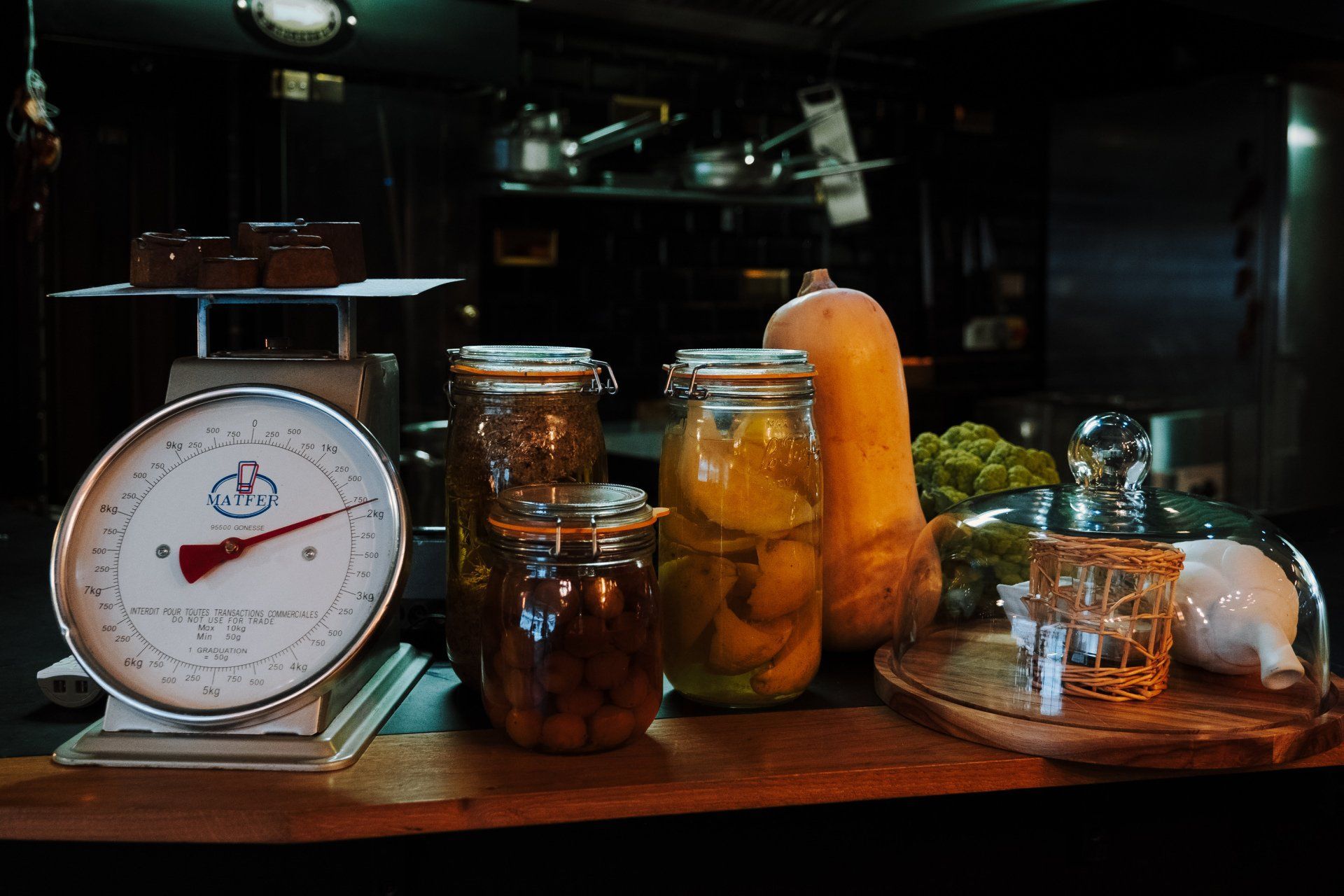 Plan de travail de cuisine avec balance, bocaux de conserves, courge et planche à découper en bois.