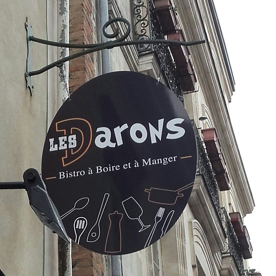 Enseigne du restaurant. Ovale noir à texte blanc, fixée sur un bâtiment en briques.