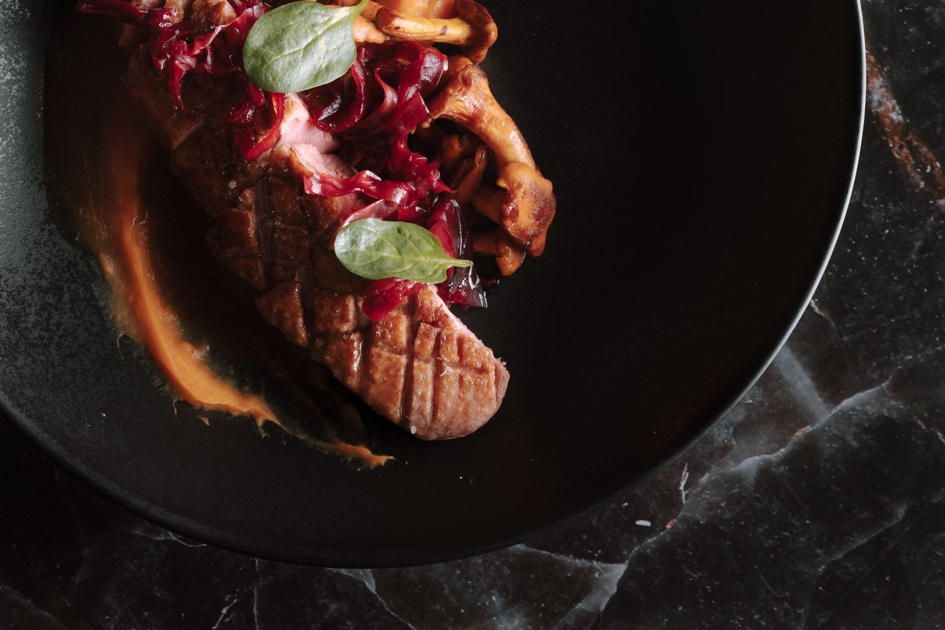 Magret de canard aux oignons rouges et à la sauce, servi sur une assiette noire.