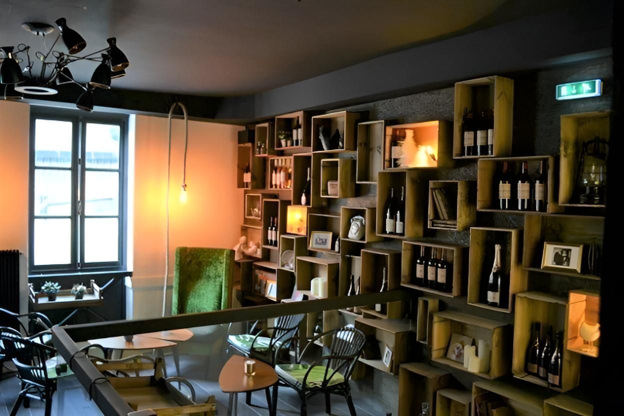 Intérieur d'un restaurant avec des bouteilles présentées dans des caisses en bois sur un mur, des tables et des chaises.