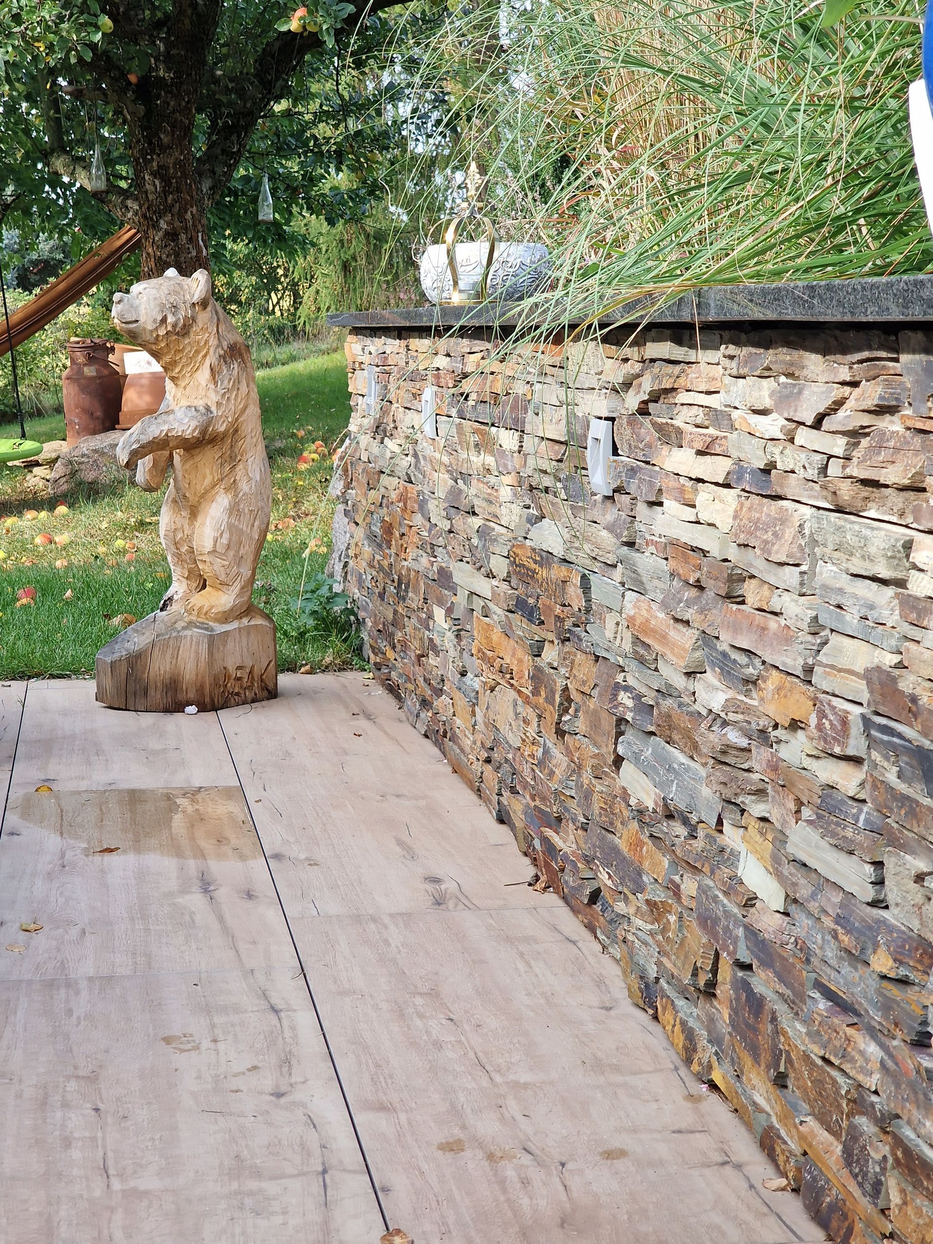 Eine Steinmauer grenzt an ein Holzdeck mit einer Bärenstatue.