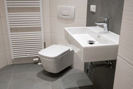 Modernes Badezimmer mit weißen Armaturen: Wandtoilette, Waschbecken und Heizkörper. Grauer Fliesenboden und Akzente.