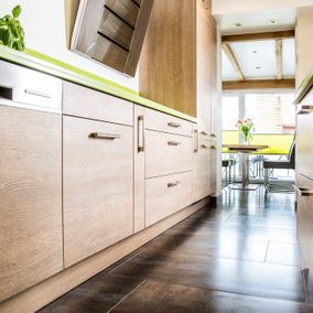 Küchenschränke aus Holz mit hellgrünen Arbeitsplatten und dunklem Fliesenboden.