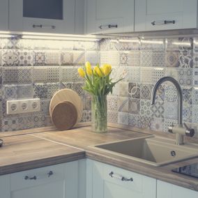 Küchenecke mit weißen Schränken, gemusterter Küchenrückwand, Holzarbeitsplatte und gelben Tulpen.