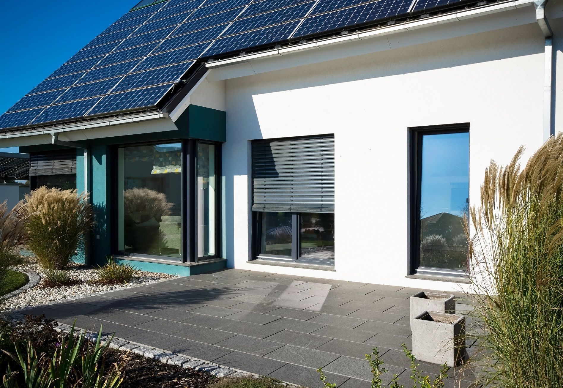 Modernes weißes Haus mit Solarzellen, Fenstern und Terrasse.