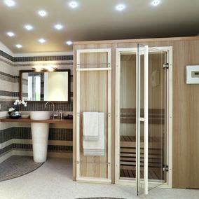 Badezimmer mit Sauna; beige und graue Fliesen, weißes Waschbecken, Holzsauna mit Glastür, sanfte Beleuchtung.