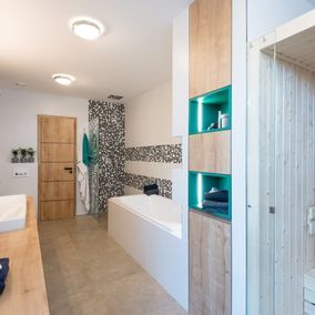 Modernes Badezimmer mit hellen Holzschränken, blaugrünen Akzenten, einer Sauna und einer Badewanne mit einer Wand aus Mosaikfliesen.