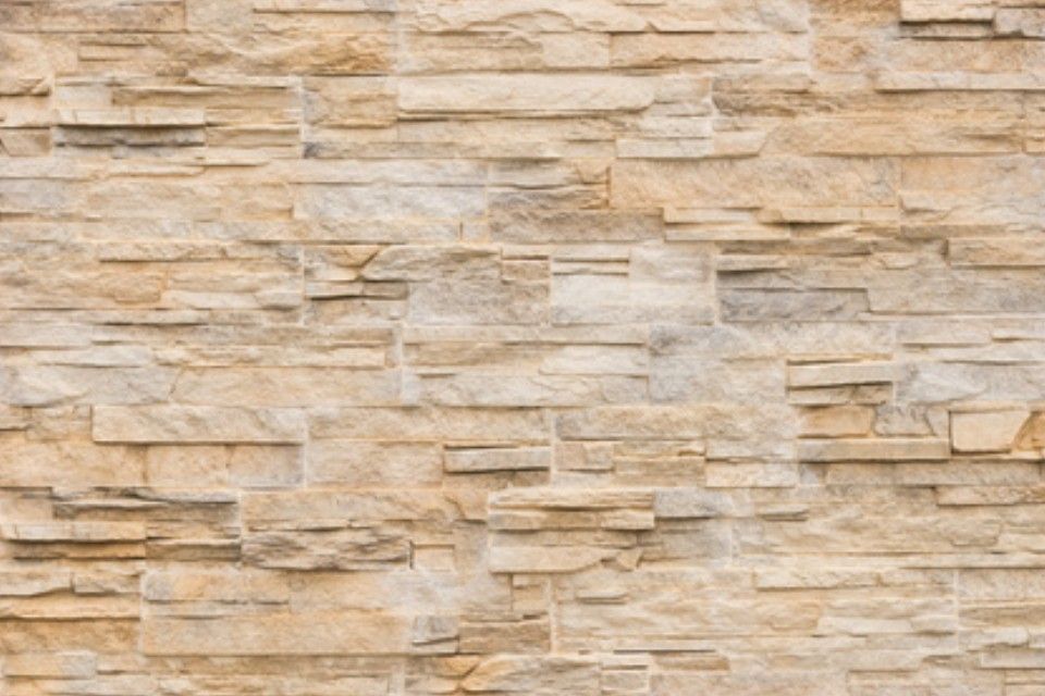 Hellbraune Steinmauer mit geschichtetem, strukturiertem Aussehen.