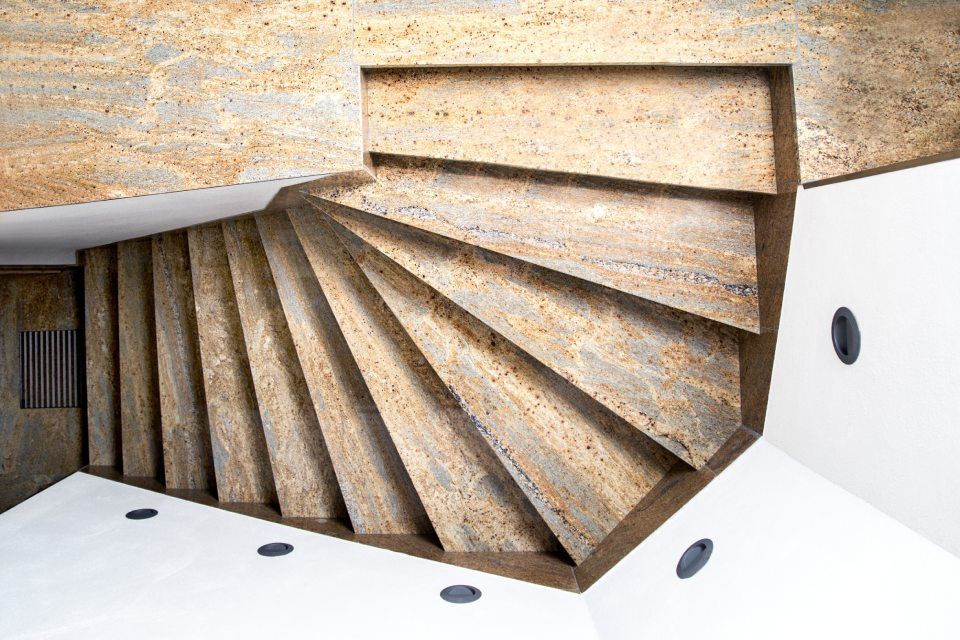 Wendeltreppe mit Steinstufen, kontrastierenden weißen Wänden und Einbauleuchten.