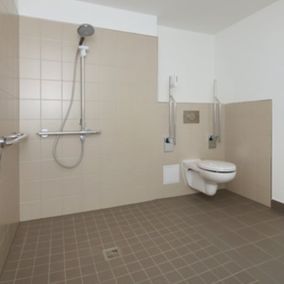 Barrierefreies Badezimmer mit Dusche, Toilette und Haltegriffen. Beige Wände und gefliester Boden.
