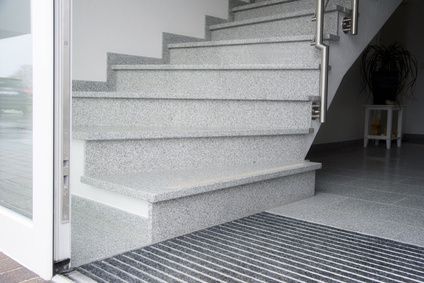 Granittreppe, die zu einem Treppenabsatz führt. Grau und weiß gesprenkelte Steinstufen mit einem Metallhandlauf auf der rechten Seite.
