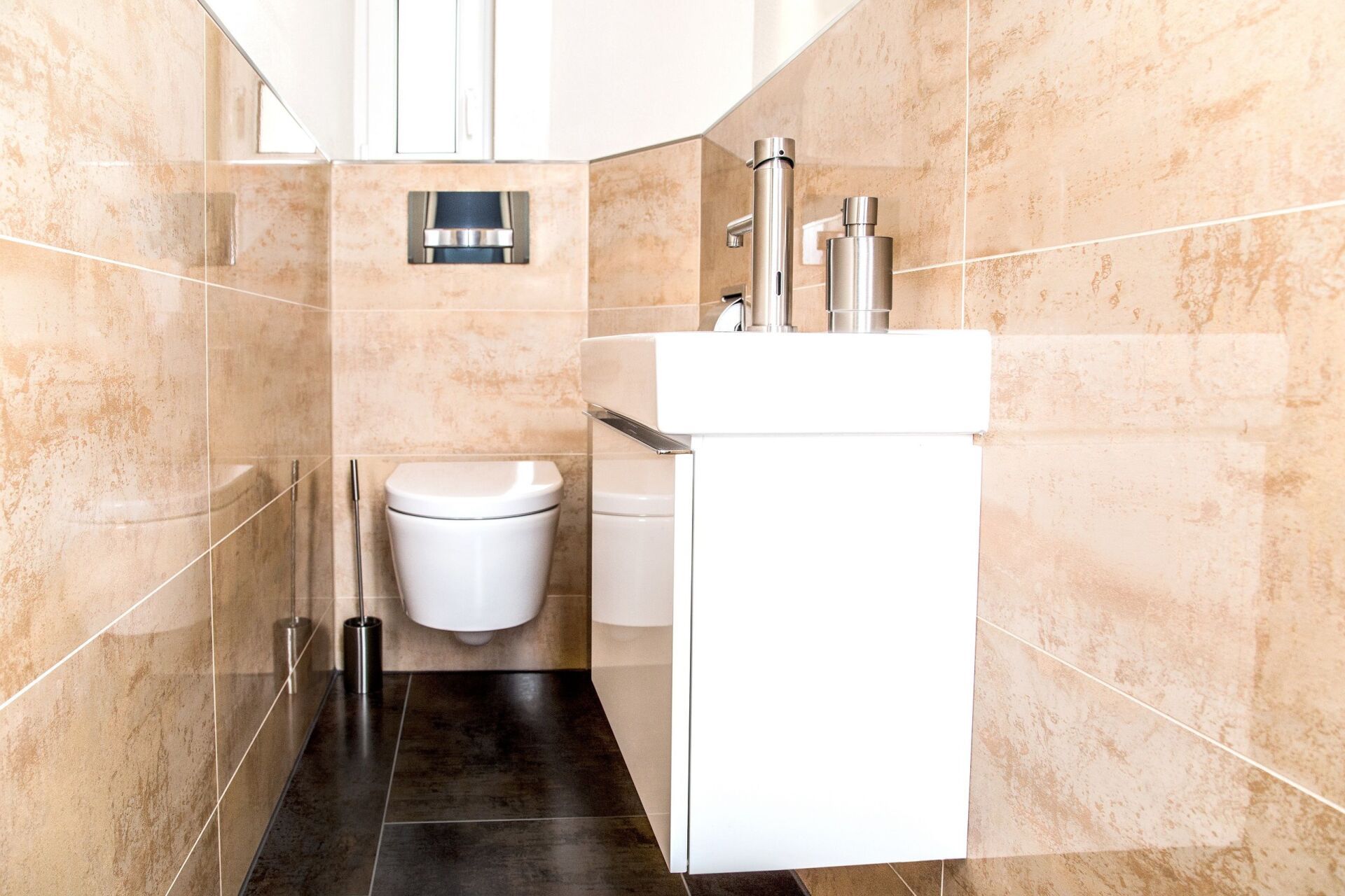 Kleines, modernes Badezimmer mit weißer Toilette und Waschbecken, beige gefliesten Wänden und schwarzem Boden.