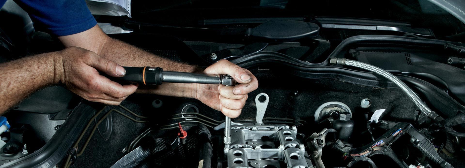 Un hombre está trabajando en el motor de un automóvil con una llave inglesa.