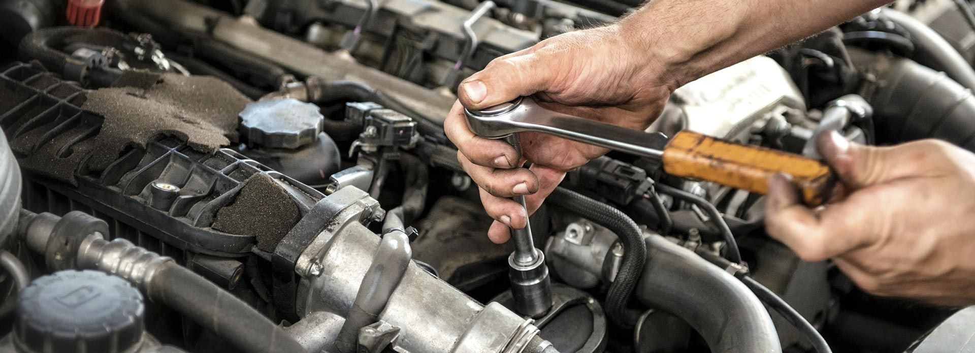 Un hombre está trabajando en el motor de un automóvil con una llave inglesa.