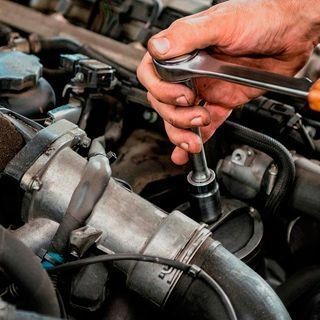 Una persona está trabajando en el motor de un automóvil con una llave inglesa.