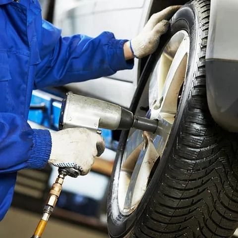 Un hombre con una chaqueta azul está usando una llave neumática para cambiar un neumático.