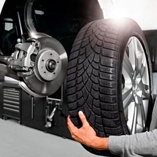 Una persona sostiene un neumático delante de un automóvil.