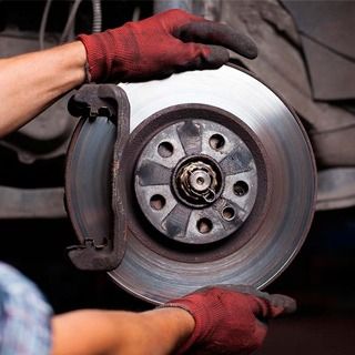 Una persona que lleva guantes rojos está arreglando un disco de freno de un coche.