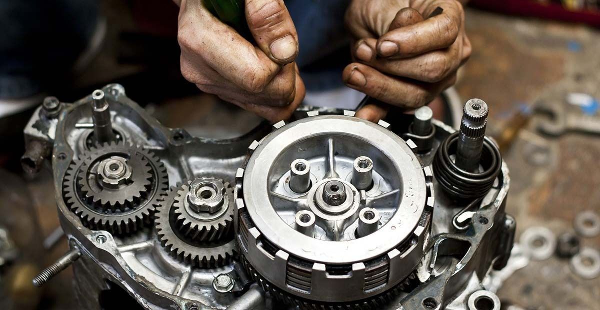 Un hombre está trabajando en el motor de una motocicleta con un destornillador.