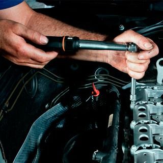 Un hombre está trabajando en el motor de un automóvil con un destornillador.