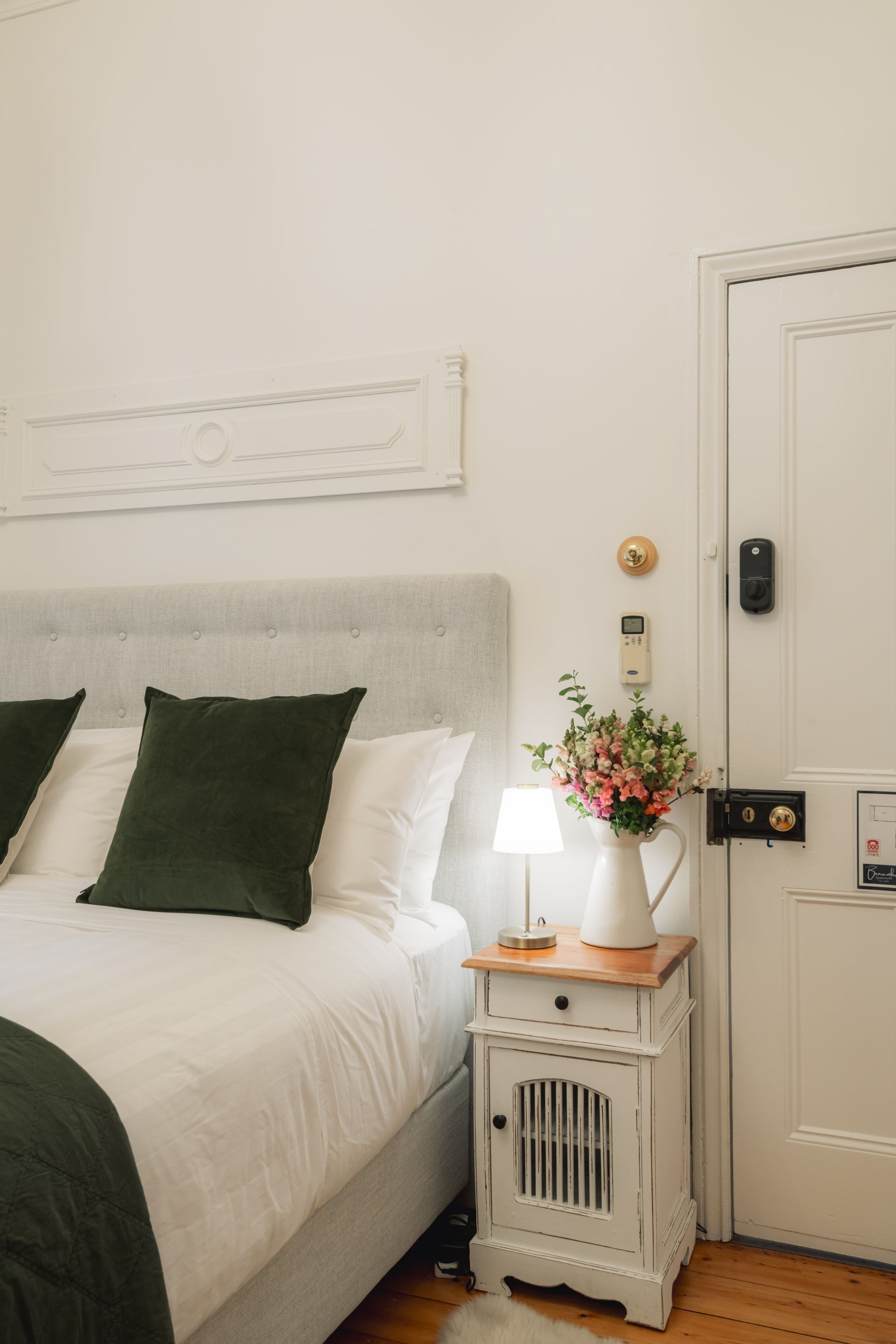 A bedroom with a bed , nightstand , lamp and vase of flowers.