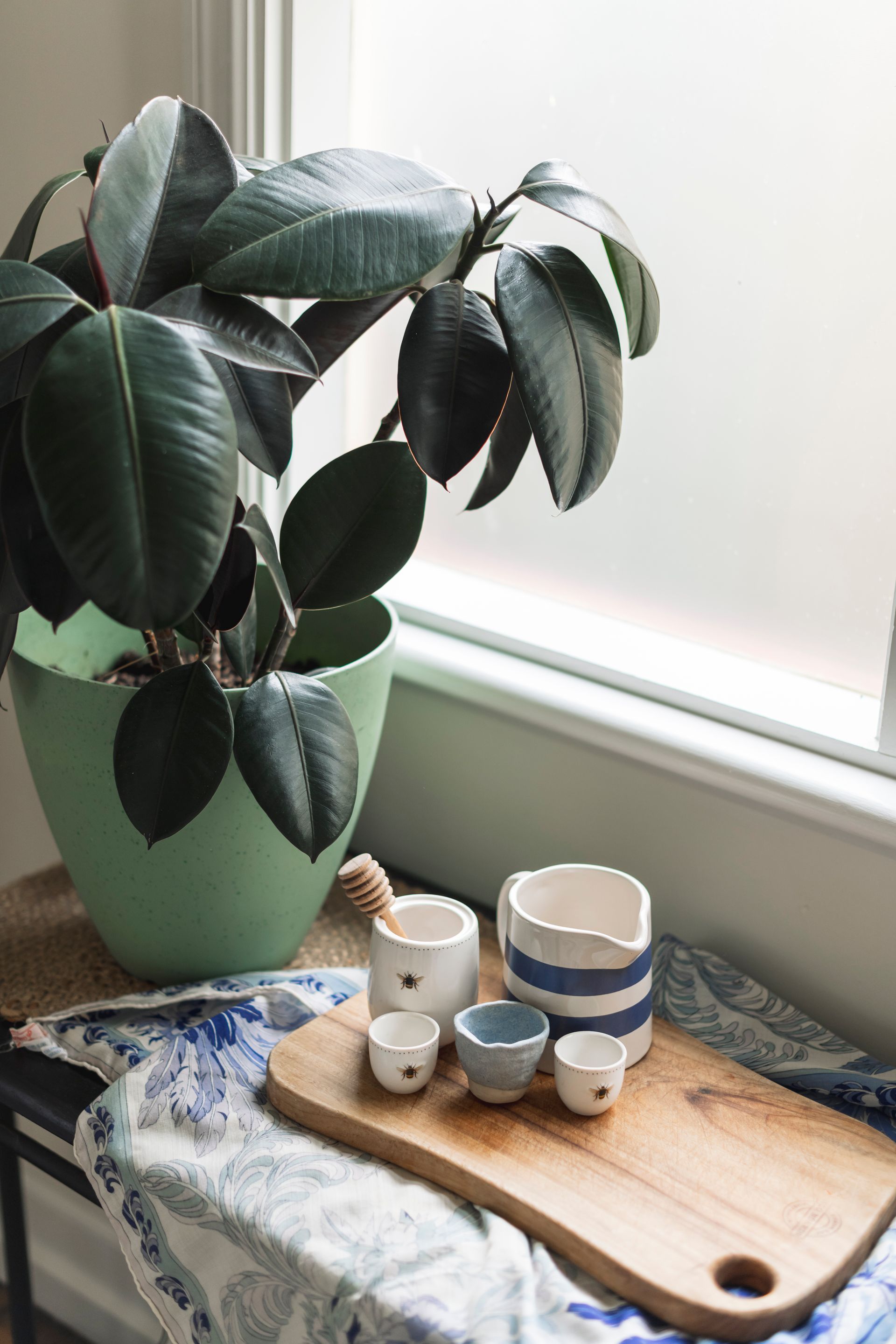 A potted plant is sitting on a wooden cutting board next to a window.